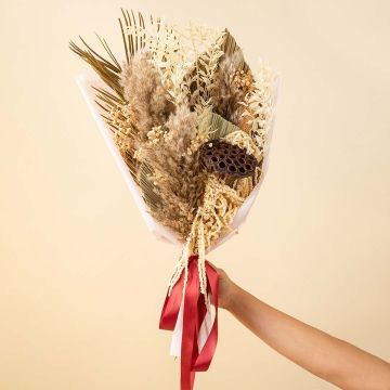 Rustic dried flower bouquet with pampas palm leaves ruscus and lotus pod wrapped with red ribbon on plain background.