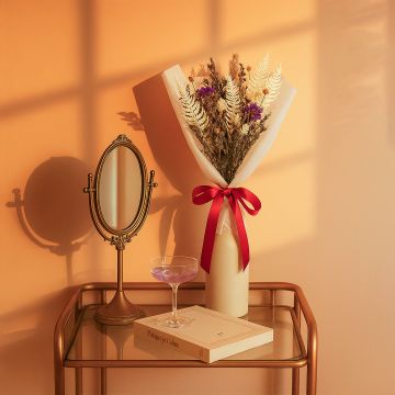 Luxury dried flower bouquet in white wrapping with red ribbon placed on golden table beside mirror for home decor styling.