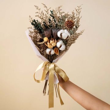 Dried flower bouquet with cotton stems lotus pod pine cone magnolia flower strawberry fruit and eucalyptus in natural tones.