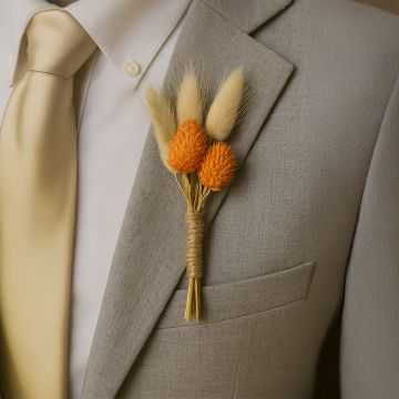 Groom wearing dried flower boutonniere with orange preserved blooms and jute wrap styled on grey suit for wedding outfit.