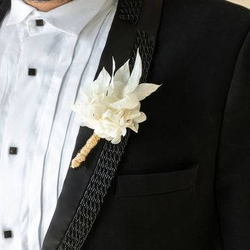 Closeup of elegant white flower boutonniere pinned on a black suit – preserved artificial wedding flower.