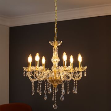 Crystal chandelier with gold frame and candle lights glowing in modern living room with dark accent wall.