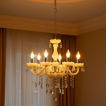 White chandelier with crystal droplets glowing warmly in living room corner creating elegant interior lighting.