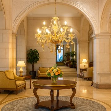 Golden chandelier with crystal droplets glowing in luxury hotel lobby above round table with floral centerpiece.