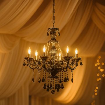 Elegant chandelier with crystal droplets glowing warmly in a luxury interior with draped curtains.