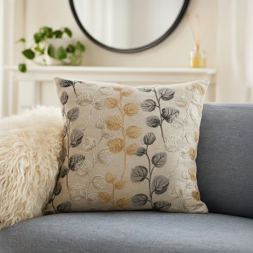 Cotton cushion with gold grey and black embroidered leaf pattern placed on a modern blue sofa creating a stylish cozy lifestyle decor accent for home interiors.