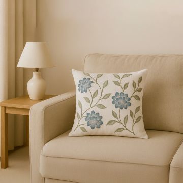 Cotton cushion with blue floral embroidery placed on a beige armchair creating a soft cozy lifestyle decor accent for warm modern living spaces.
