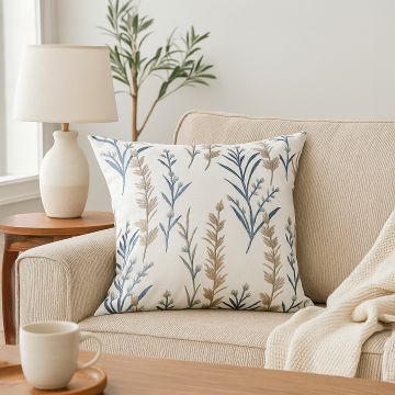 Cream sofa styled with a beige embroidered cushion featuring blue and gold botanical patterns creating a cozy modern lifestyle home decor accent.