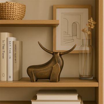 Decorative bronze bull figurine displayed on a wooden shelf next to stacked books a glass vase with dried stems and a framed minimalist line artwork creating a warm modern home decor setting.