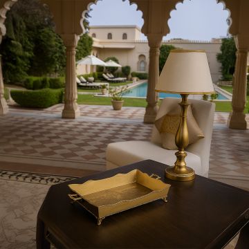 A gold decorative serving tray placed on a dark wooden table in a luxurious outdoor seating area overlooking a pool and landscaped garden during the day.