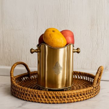 Elegant brass fruit holder filled with fresh apples and mangoes displayed on a woven rattan tray on a marble counter creating a warm homely lifestyle setting.