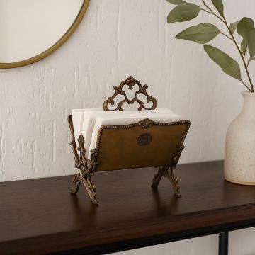 Decorative brass napkin stand with baroque style handle placed on console with vase and mirror in warm setting.
