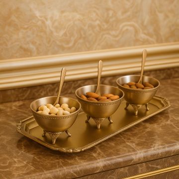 Elegant three bowl brass snack serving set displayed on a marble counter with decorative wall detailing creating a luxurious lifestyle presentation.