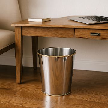 A polished metal waste bin placed neatly under a wooden desk in a warm home office setting with soft natural light enhancing the elegant metallic finish of the bin.