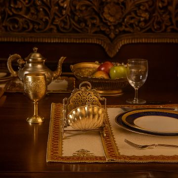 Antique gold brass folding biscuit warmer with shell design on a dining table with matching brass tableware for a royal vintage home decor theme.