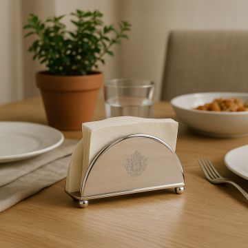 Elegant silver plated semi circular napkin holder with ball feet holding tissues on a wooden dining table with a potted plant and plates.