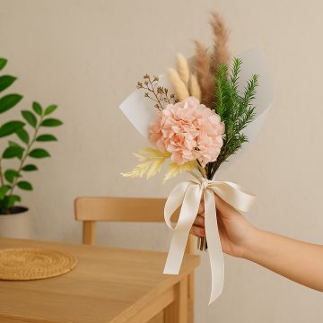 Lifestyle preserved flower bouquet with pink hydrangea pampas grass lotus pod and greenery wrapped with satin ribbon creating rustic table decor.