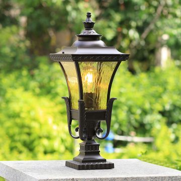 Elegant outdoor pillar light in black metal with glass shade glowing warmly in garden decor for pathway and patio lighting.