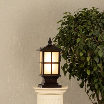 Black metal outdoor post lantern Light On mounted on a stone pillar Traditional garden gate lighting Main Lifestyle image at night.