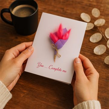 Romantic greeting card with pink dried flowers held in hand on wooden table beside coffee cup for cozy gifting moment.