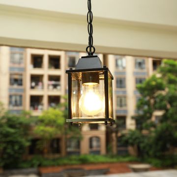A compact black outdoor hanging lantern with light on glowing warmly against a blurred garden and building backdrop adding charm and brightness to the balcony space.