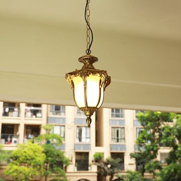 Black metal outdoor pendant light hanging on a porch ceiling with warm light on creating an inviting glow against a blurred building background.