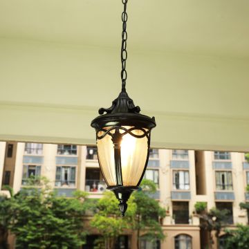 Black metal round cage pendant light hanging from a modern pergola ceiling with warm light on against a blue evening sky.