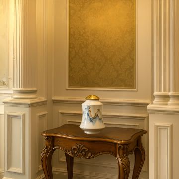 Elegant white ceramic jar with gold lid placed on a carved wooden console table enhancing classic hallway décor with a refined luxurious accent for upscale interior styling.