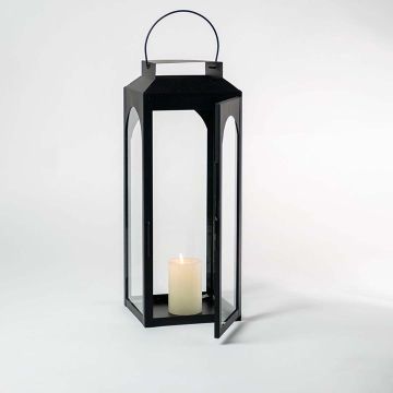 Black lantern with candle lit and glass panels displayed on white background for indoor outdoor styling.