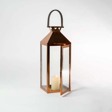 Bronze lantern photographed on a white background with soft candlelight glowing inside emphasizing the refined metallic tone and minimalist craftsmanship.