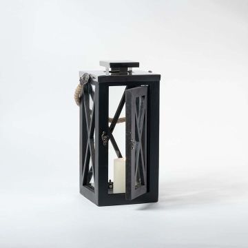 Black lantern illuminated on a clean white background highlighting its warm candle glow through clear glass sides.