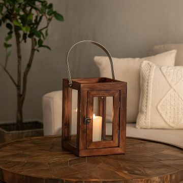 Small wooden and glass lantern with metal handle styled on wooden table adds warm rustic charm to cozy interiors.
