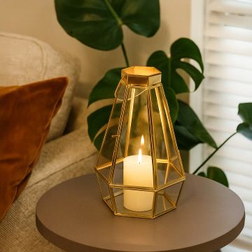 Decorative gold glass candle holder placed on a round side table beside a sofa  styled with warm lighting and indoor green plants.
