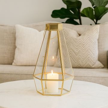 Gold metal and glass tapered lantern placed on a white marble table with the candle on creating a warm cozy accent for modern living room decor.