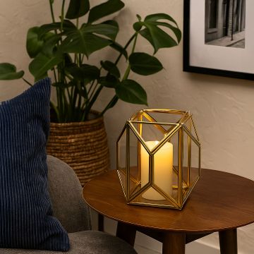 Gold metal and glass geometric lantern placed on a wooden side table with candle on creating a warm cozy accent for modern living room decor.