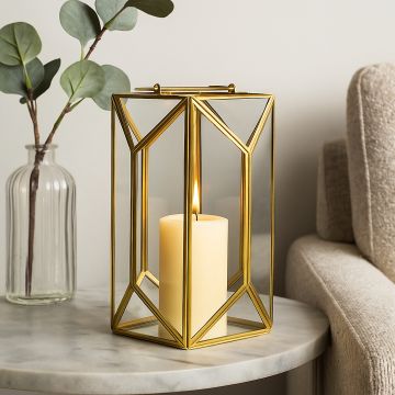 Gold metal and glass geometric candle lantern displayed on a marble side table with a lit pillar candle creating a warm cozy decor accent for living spaces.