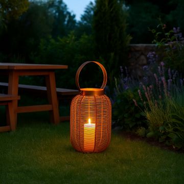 Copper metal wire mesh lantern with candle light glowing on outdoor garden lawn next to lavender plants and wooden furniture.