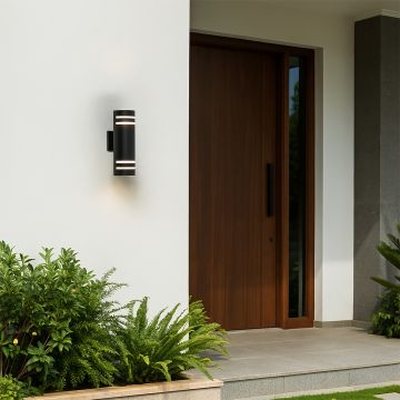 Tall black cylindrical wall light illuminating an outdoor wall with soft glow and elegant dual silver ring design.