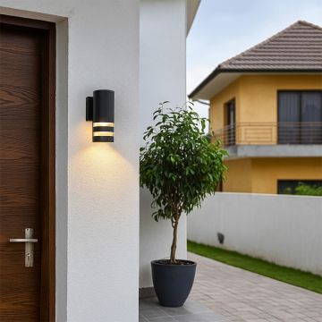 Modern black cylindrical wall light illuminating exterior walls with a sleek contemporary glow.