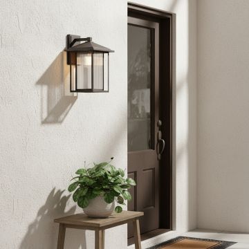 Outdoor black wall lantern installed on a house exterior illuminating the entrance with warm light.