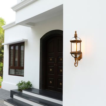 Antique bronze outdoor wall lantern with warm light on mounted next to a dark wood front door on a white stucco house.