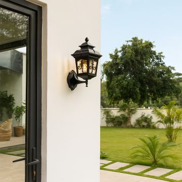 A classic black outdoor wall lantern glowing warmly beside a modern home entrance enhancing the garden view with its elegant vintage design at dusk.