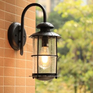 Black outdoor wall lantern with curved arm and raindrop glass creating a modern warm look in a simple lifestyle setting.