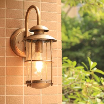 Gold outdoor wall lantern with curved arm and clear glass body creating a warm elegant look in a simple setting.