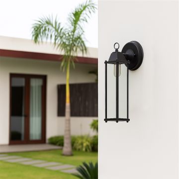 Black outdoor lantern mounted on a wall in a minimal lifestyle setting with a clear glass body and warm glowing bulb.