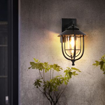 Black outdoor wall lantern styled in a soft lifestyle setting showing its curved metal frame and clear glass shade for an elegant exterior look.