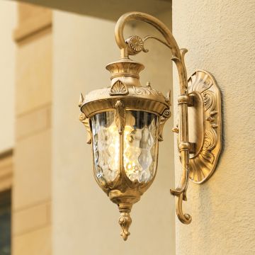 A gold antique wall lantern with the light on illuminating the exterior wall and casting a warm glow across the entrance creating an elegant and inviting outdoor ambiance.
