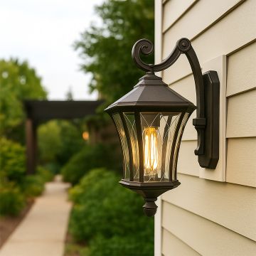 A black outdoor wall lantern with the light on illuminating the siding and garden walkway creating a warm welcoming ambiance with soft glow enhancing the modern home exterior.