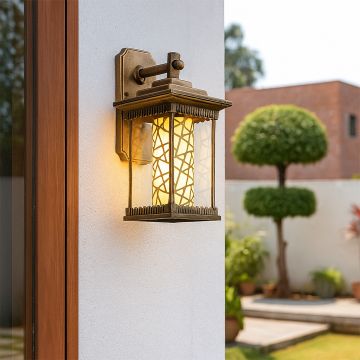 Gold metal outdoor lantern with patterned glass glowing warmly on a white exterior wall creating a welcoming and elegant outdoor lifestyle ambience.