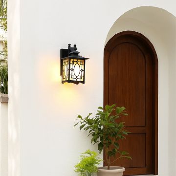 Black metal outdoor lantern with oval patterned frosted glass glowing warmly beside an arched wooden door creating a cozy inviting exterior ambience.